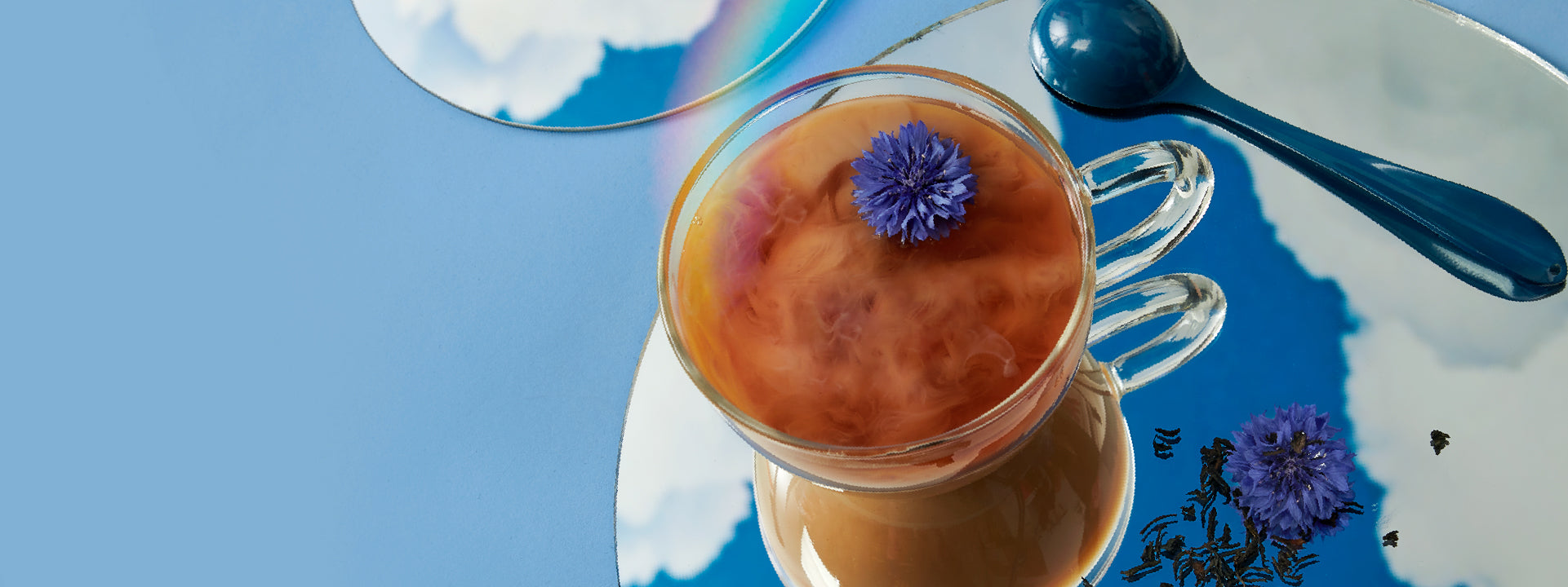 Clear cup of black tea with a splash of milk on a blue background.