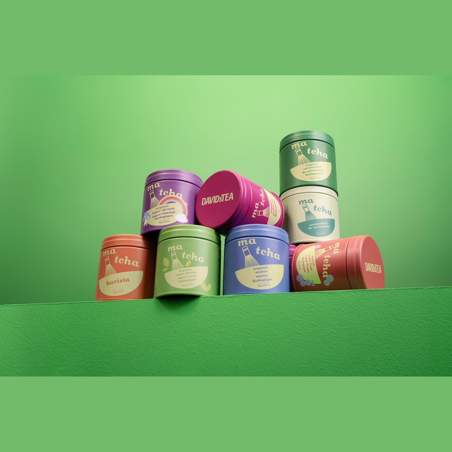 Assorted DAVIDsTEA matcha tea tins stacked together on a green background